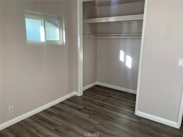 a view of an empty room with wooden floor & a window