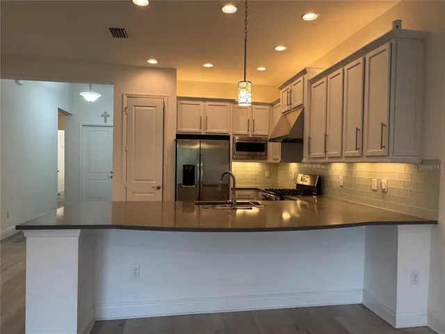 a kitchen with stainless steel appliances granite countertop a refrigerator a stove and a sink with wooden floor