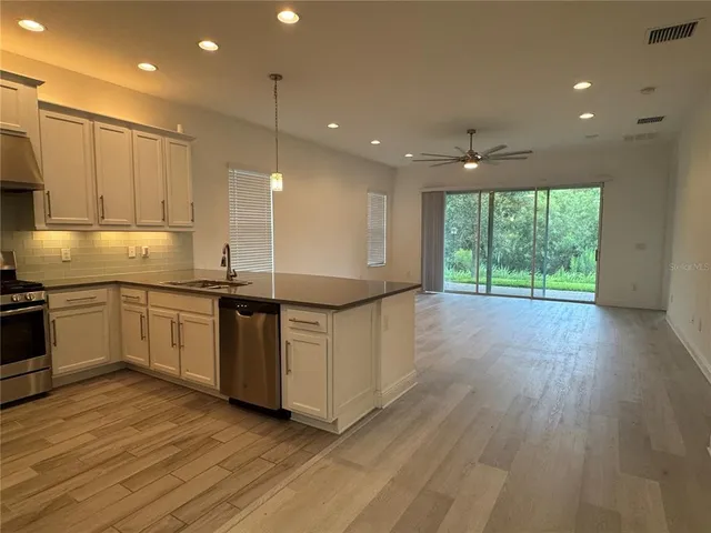 a kitchen with stainless steel appliances granite countertop a stove a sink and white cabinets with wooden floor