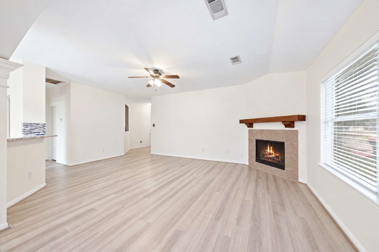 6911 River Road Richmond, TX 77469 - Photo 10 of 36 Anchored by a corner fireplace with a warm wood mantle, the expansive living room offers durable wood-look flooring and a light-filled open concept. Wide windows with custom blinds frame views of the outdoors, while the direct pass-through to the kitchen breakfast bar ensures seamless everyday entertaining.
