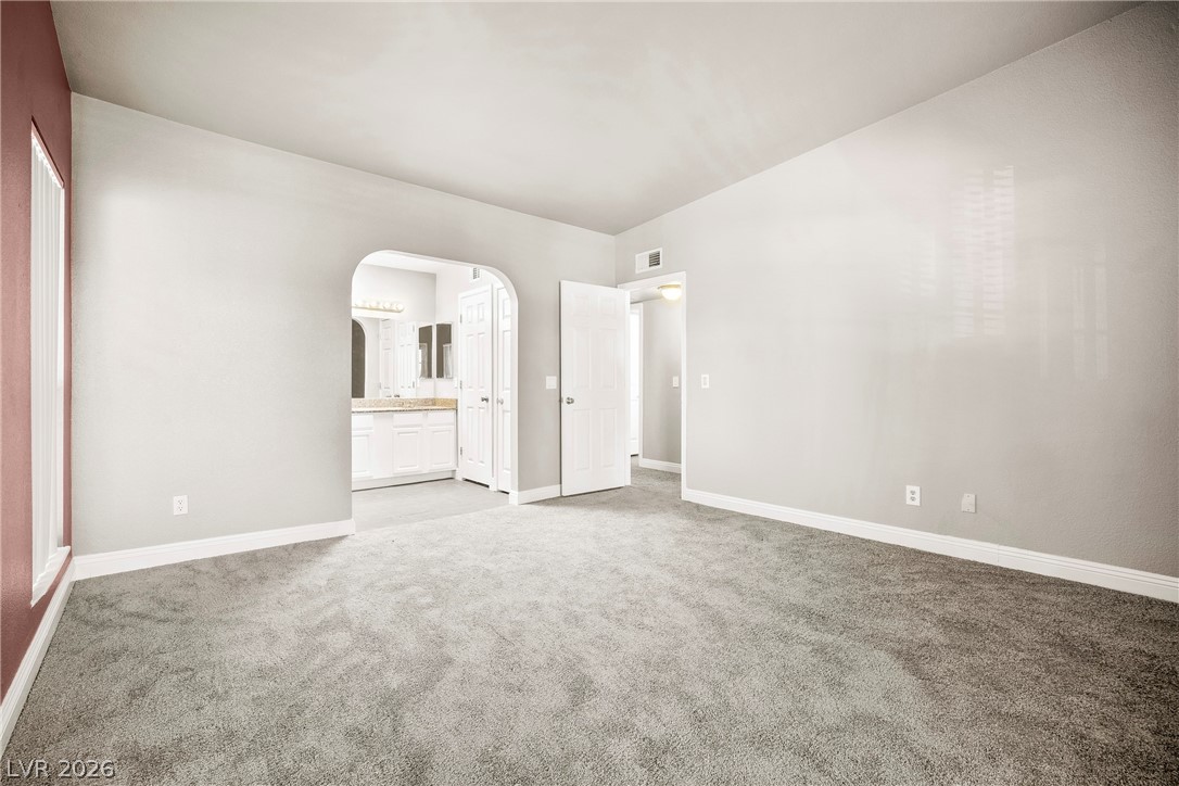 3311 Sunfish Drive, Unit D Henderson, NV 89014 - Photo 12 of 21 A spacious room offers comfortable gray carpeting and an arched entry leading to a well-appointed primary bathroom.