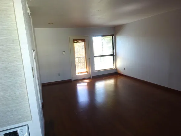 an empty room with wooden floor and windows with curtains