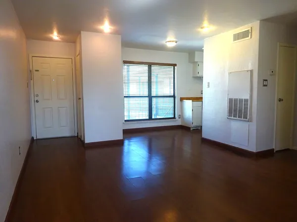 an empty room with wooden floor and windows with curtains