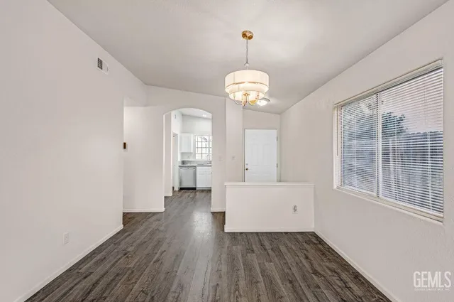 a view of a room with wooden floor chandeliers and kitchen view
