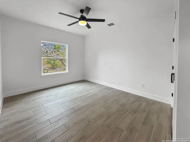 an empty room with wooden floor ceiling fan and windows