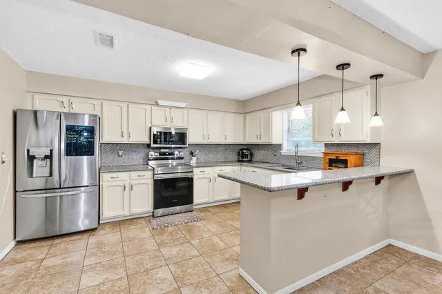 a kitchen with stainless steel appliances granite countertop a refrigerator a stove a sink and a chandelier