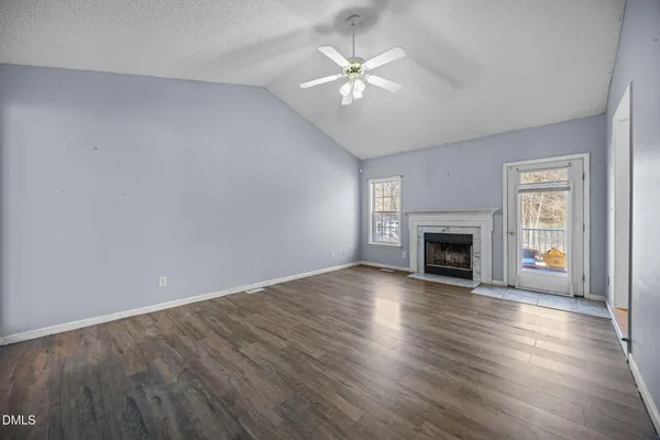 an empty room with wooden floor fireplace and windows