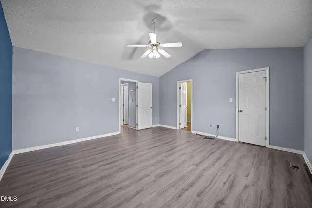 a view of an empty room with wooden floor and a ceiling fan