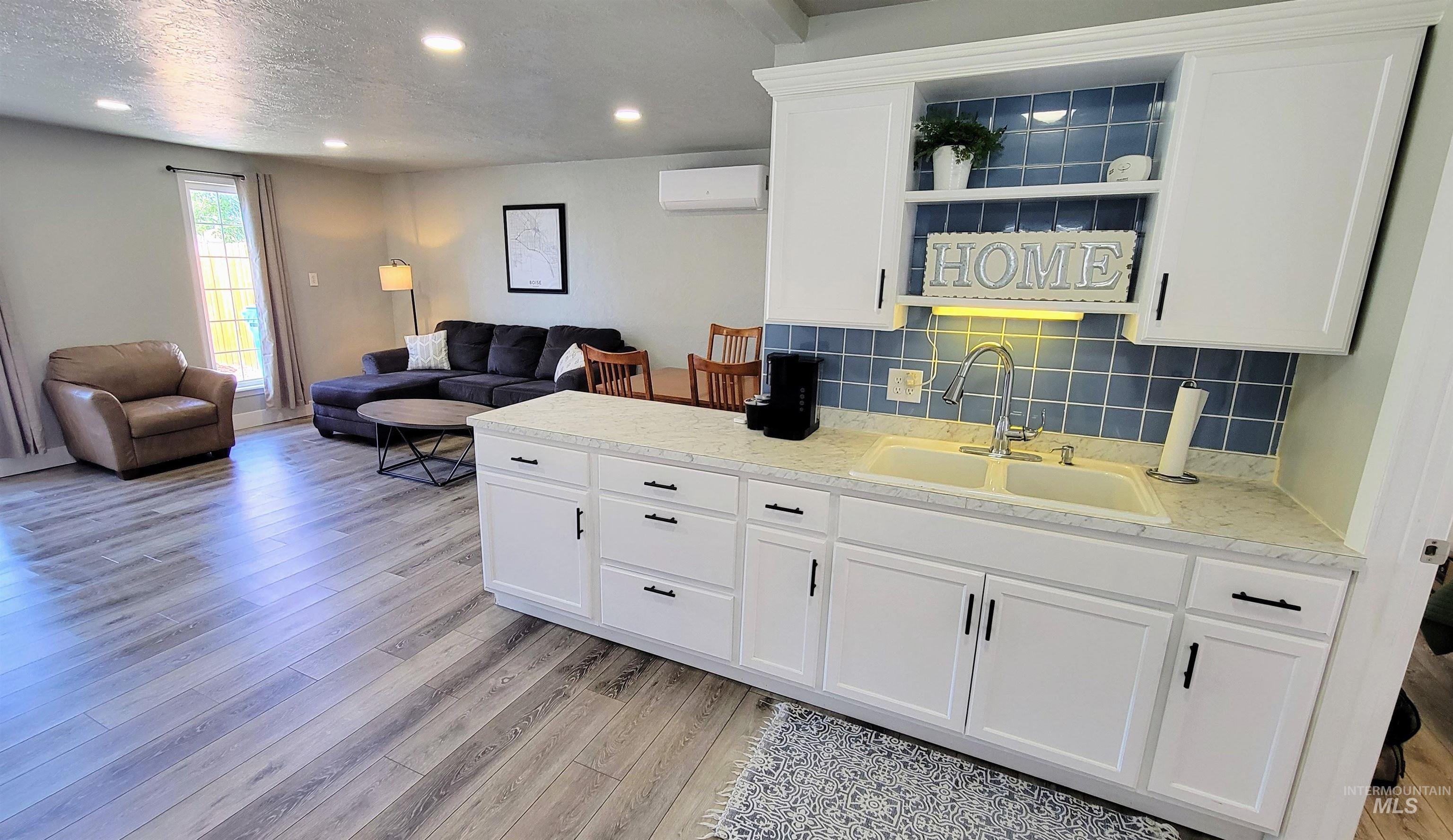 814 Baker Street Boise, ID 83706 - Photo 17 of 26 Open-concept living space featuring wood-finish flooring, recessed lighting, and a kitchen area with white cabinetry, a light-colored countertop, and a blue tiled backsplash