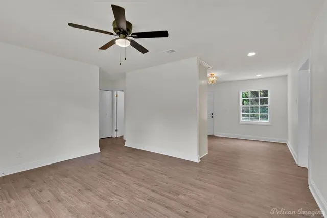 a view of an empty room with wooden floor and a ceiling fan