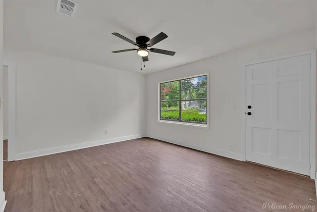 an empty room with wooden floor fan and windows