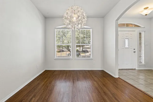 an empty room with wooden floor chandelier and windows