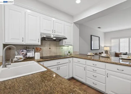 a kitchen with stainless steel appliances granite countertop a stove a sink a refrigerator and white cabinets with wooden floor