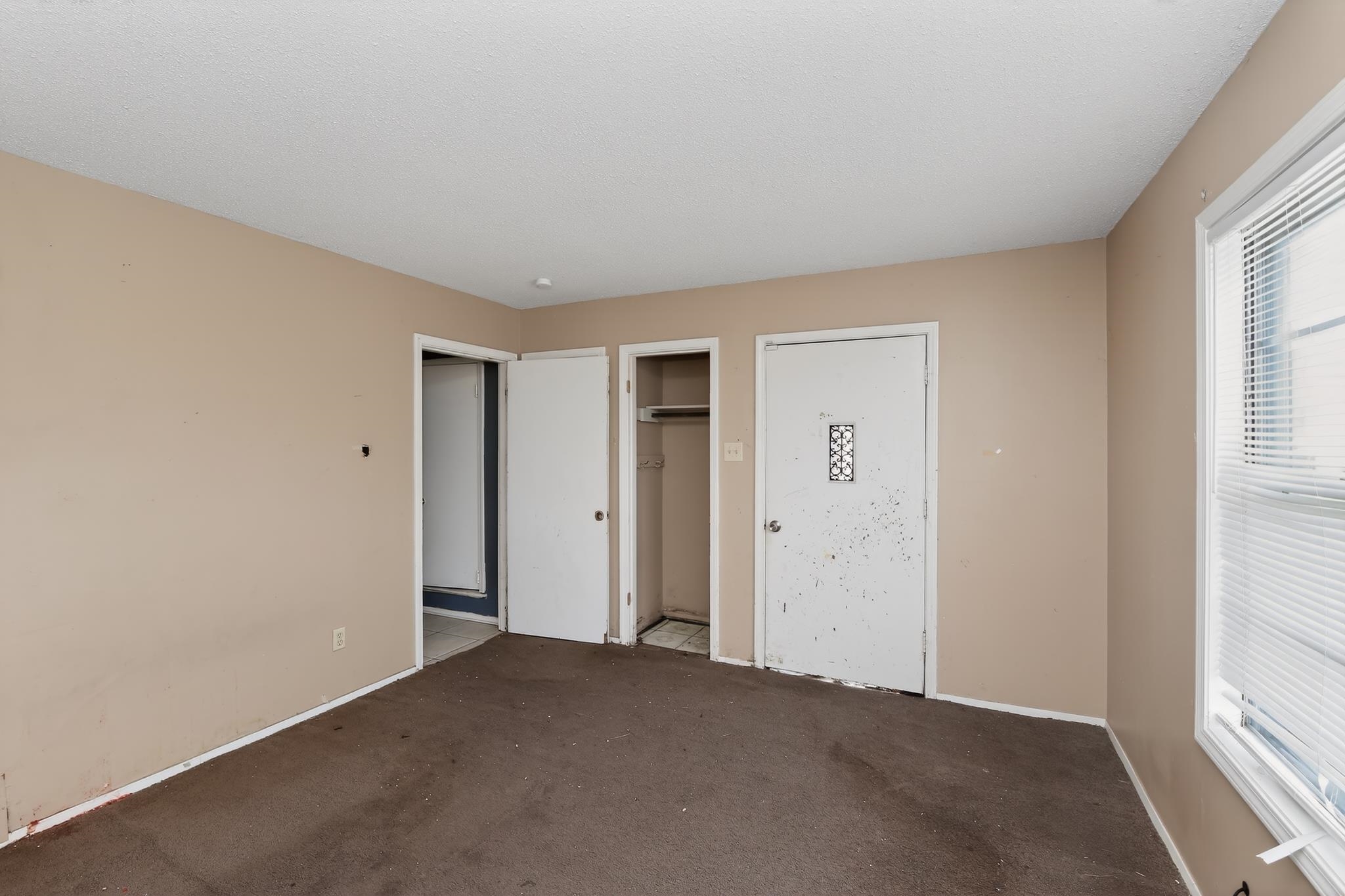 645 Parkrose Road Memphis, TN 38109 - Photo 15 of 32 Carpeted interior space featuring beige walls, multiple doorways, and a window with horizontal blinds