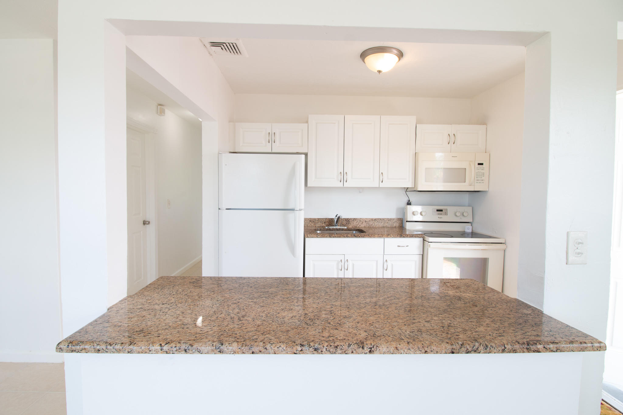 1031 West 3rd Street Riviera Beach, FL 33404 - Photo 9 of 11 a kitchen with granite countertop a refrigerator a stove a sink and white cabinets