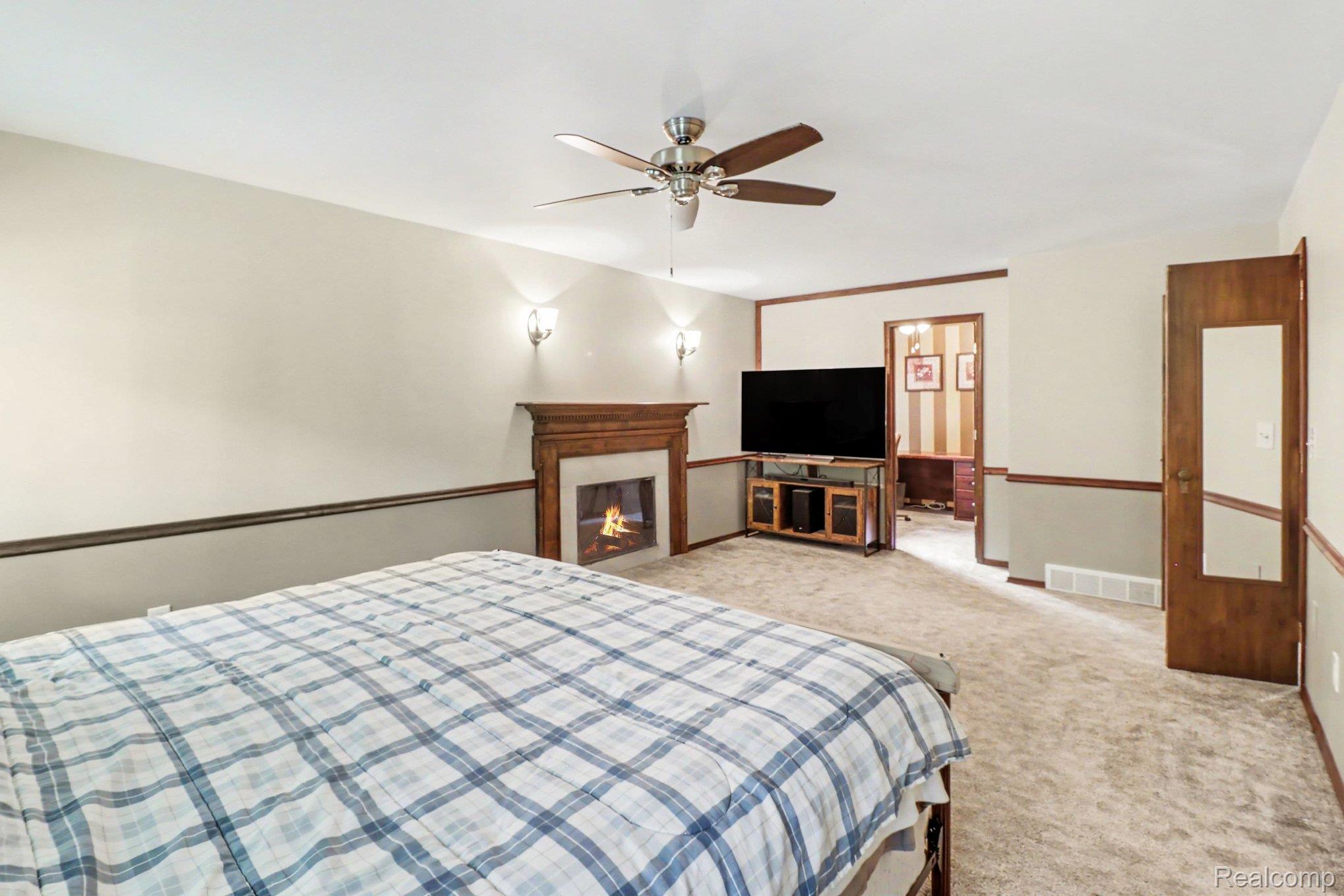 6300 North Raddatz Road Fowlerville, MI 48836 - Photo 20 of 42 Recessed fireplace with wood mantel, wall sconce lighting, ceiling fan, and carpet flooring