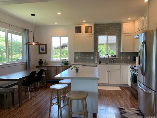 a kitchen with stainless steel appliances granite countertop a stove a sink a microwave refrigerator and chairs with wooden floor