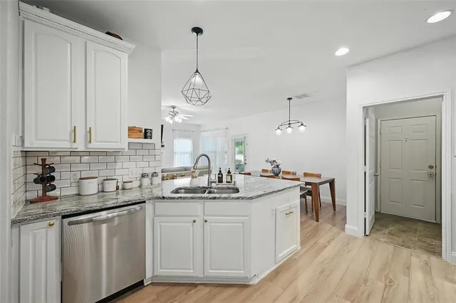 a kitchen with a sink dishwasher and white cabinets with wooden floor