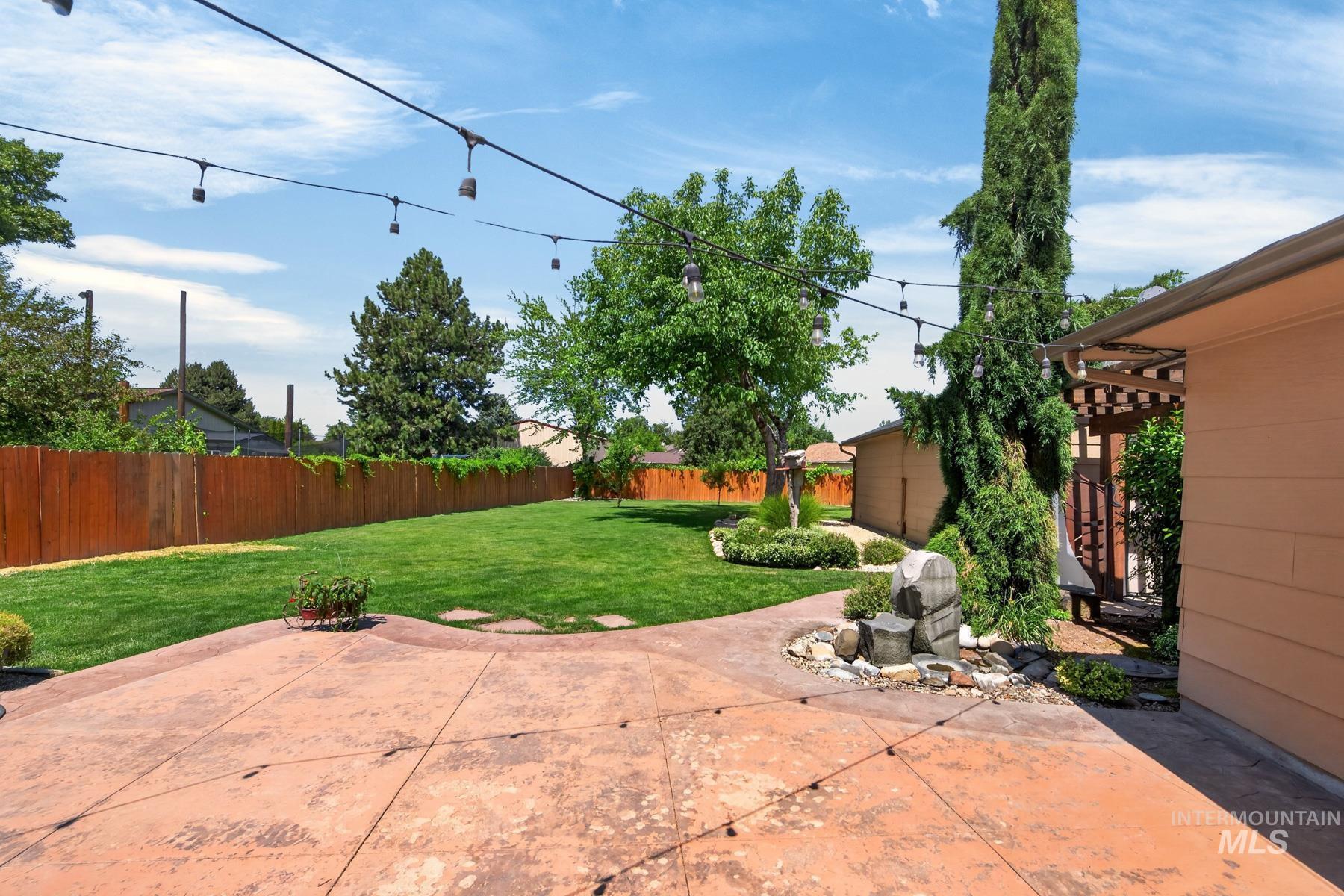 9622 Delaware Street Boise, ID 83709 - Photo 31 of 48 Expansive backyard featuring a stamped concrete patio, mature trees, string lighting, a manicured lawn, and a wooden privacy fence