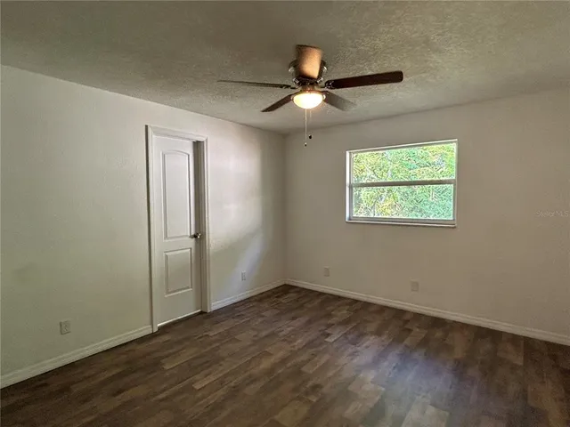 an empty room with wooden floor chandelier fan and windows
