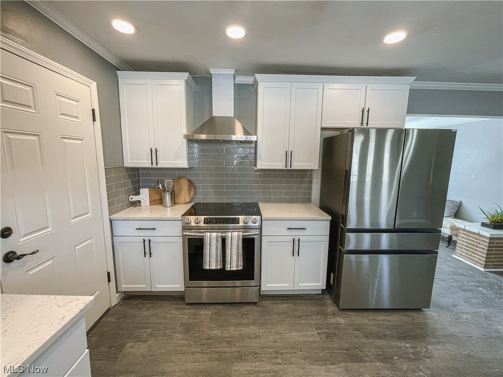 24709 Emery Road Warrensville Heights, OH 44128 - Photo 9 of 34 Kitchen featuring backsplash, dark wood-type flooring, white cabinetry, appliances with stainless steel finishes, and wall chimney exhaust hood