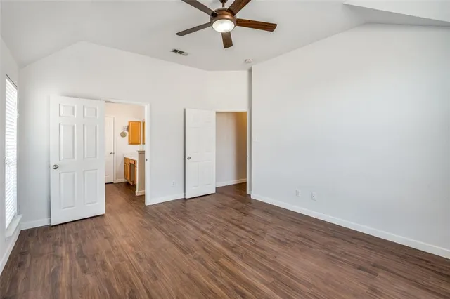 an empty room with wooden floor ceiling fan and windows