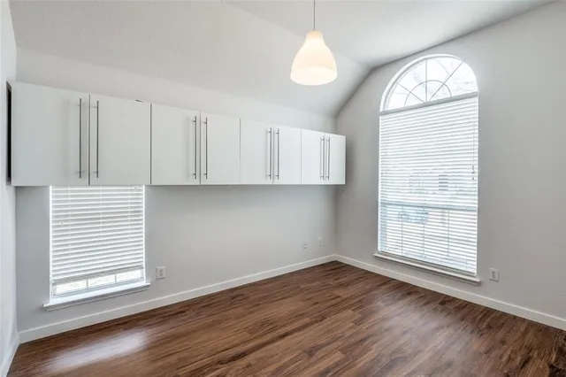 an empty room with wooden floor cabinet and windows