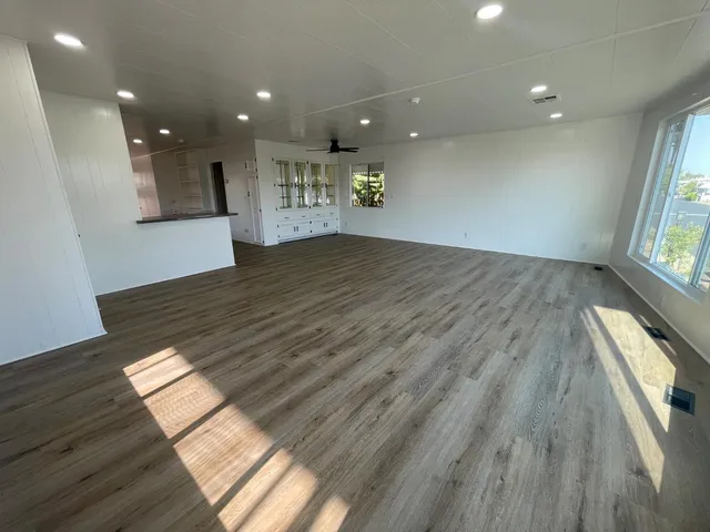 a view of kitchen and an empty room with wooden floor and windows