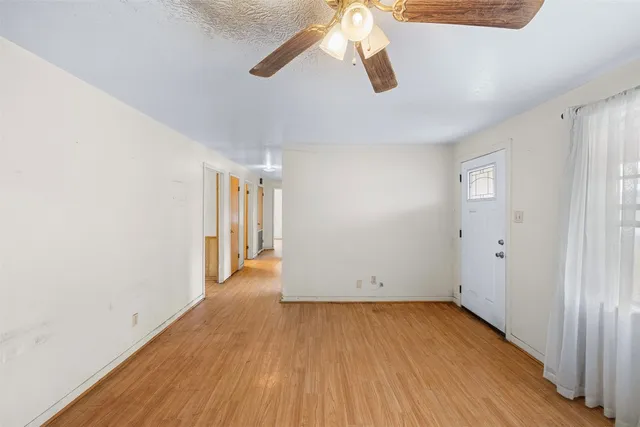 an empty room with wooden floor chandelier fan and windows
