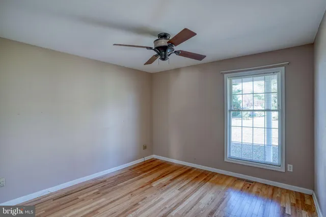 an empty room with wooden floor ceiling fan and windows