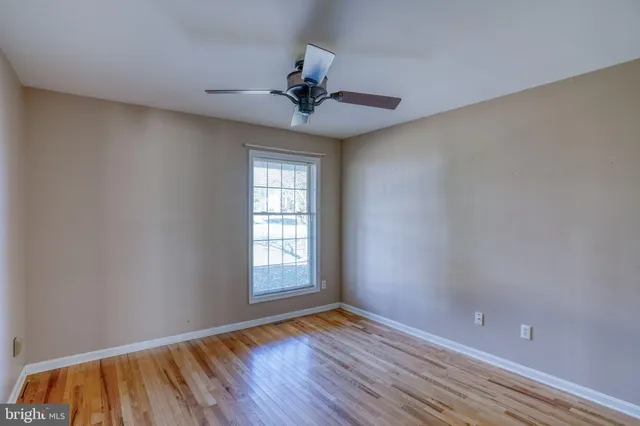 an empty room with wooden floor chandelier fan and windows