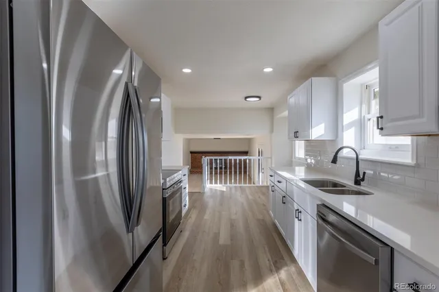 a kitchen with stainless steel appliances granite countertop a refrigerator a sink a stove and white cabinets