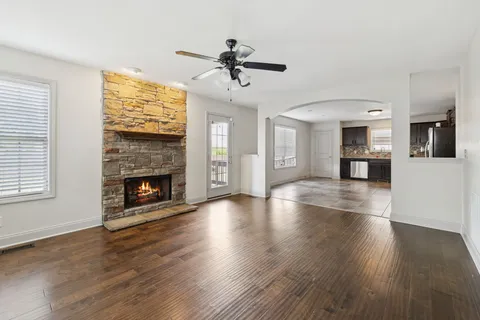 a view of a livingroom with a fireplace a ceiling fan and windows