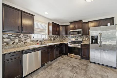 a kitchen with stainless steel appliances granite countertop a stove top oven a sink and dishwasher a refrigerator with wooden floor