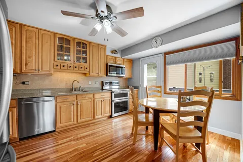 a kitchen with stainless steel appliances granite countertop a stove top oven a sink dishwasher a dining table and chairs with wooden floor