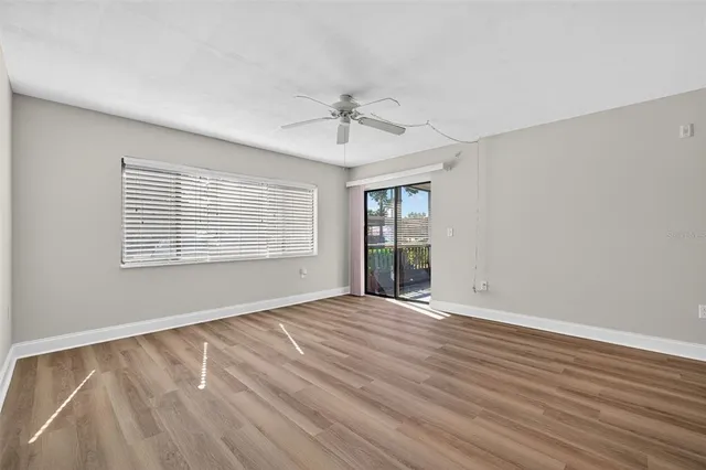 a view of an empty room with wooden floor and a ceiling fan