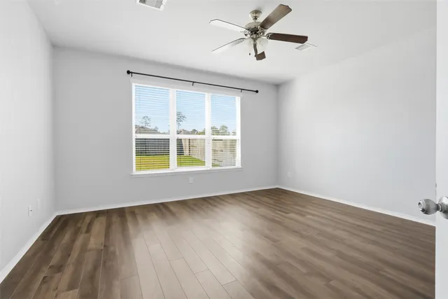 an empty room with wooden floor windows and fan