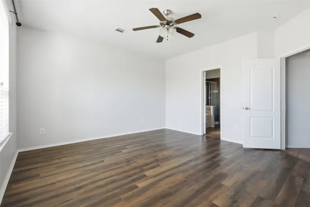 a view of an empty room with wooden floor and a ceiling fan