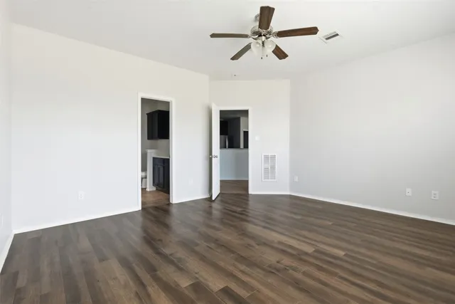 a view of an empty room with wooden floor and a ceiling fan