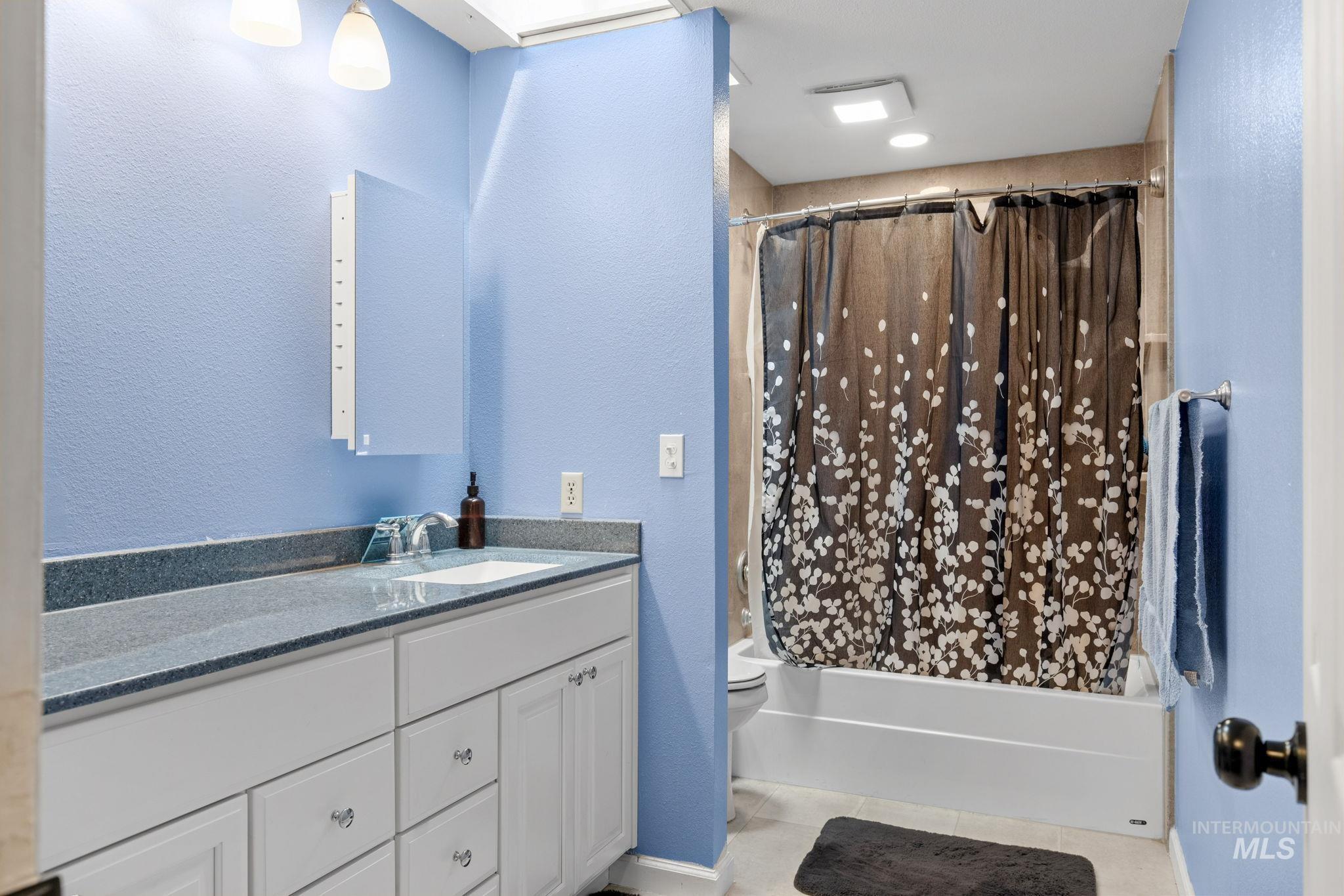 18338 Pride Lane Caldwell, ID 83607 - Photo 33 of 50 Bathroom featuring a single vanity with a solid surface countertop, white cabinetry, a built-in medicine cabinet, a full-size bathtub with a shower combination, and light-colored flooring