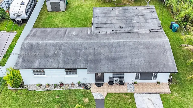 a view of a white house with a yard plants and palm trees