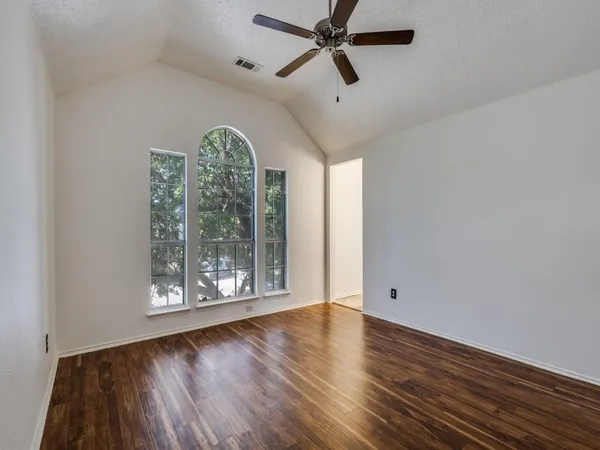 an empty room with wooden floor fan and windows