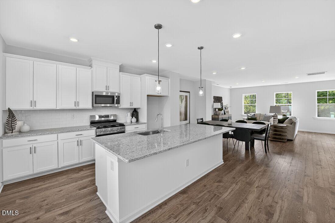 1324 West Garner Road, Unit 101 Garner, NC 27529 - Photo 9 of 29 a large white kitchen with stainless steel appliances granite countertop a stove a sink a dining table and chairs with wooden floor