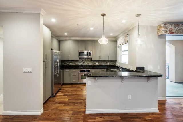 a kitchen with stainless steel appliances granite countertop a sink a stove and a wooden floors