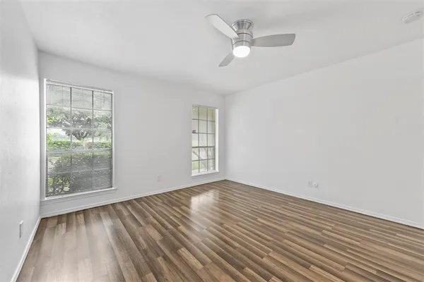 an empty room with wooden floor fan and windows