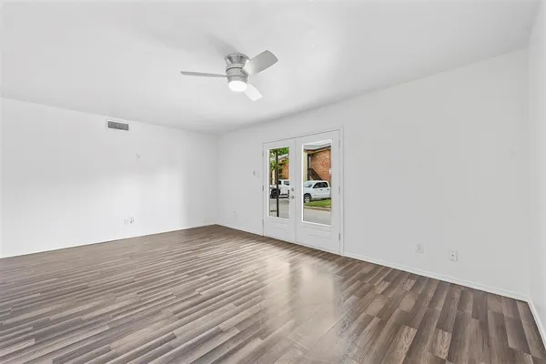 an empty room with wooden floor chandelier fan and windows