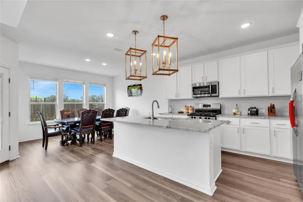 a kitchen with stainless steel appliances granite countertop a stove top oven a sink a dining table and chairs with wooden floor