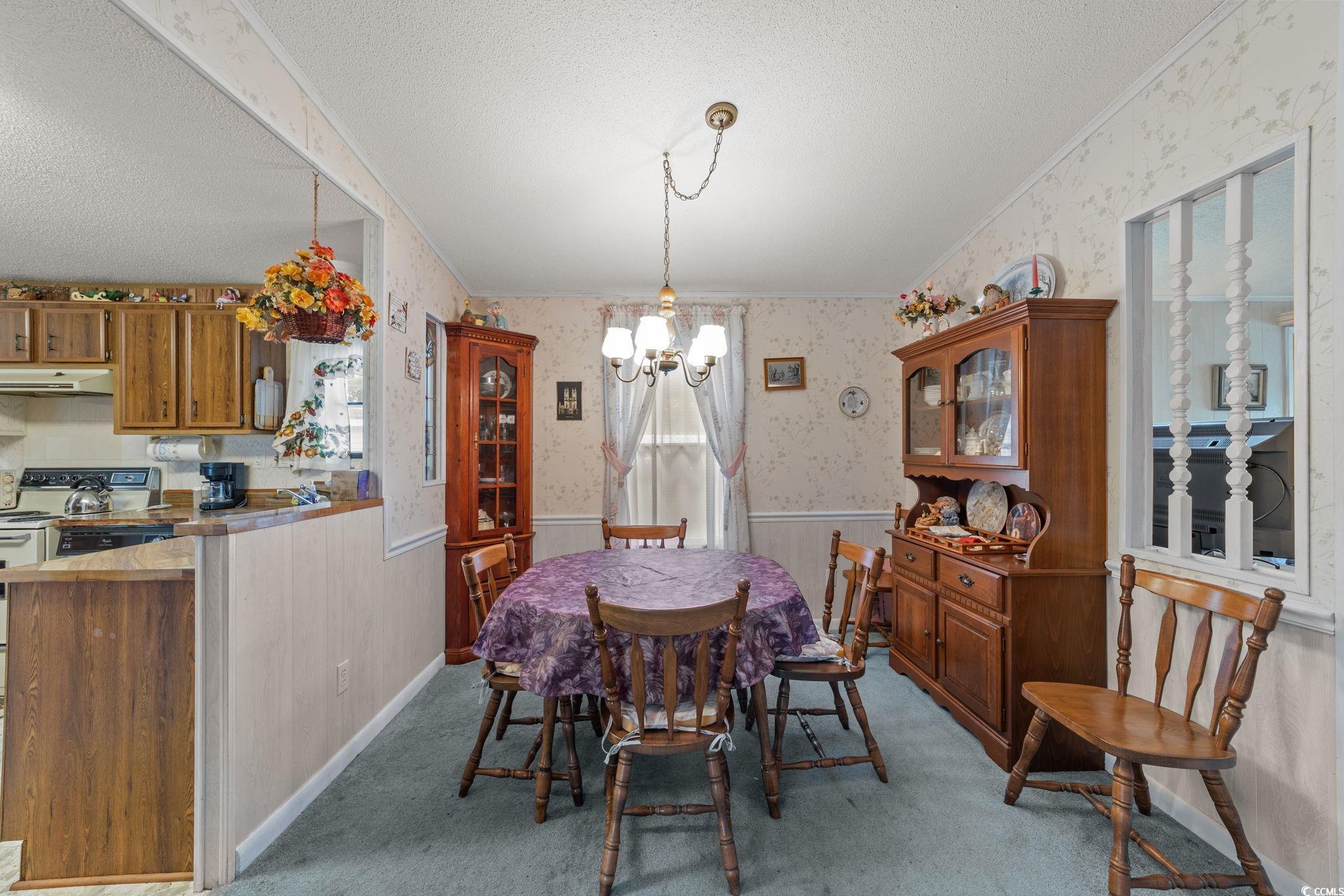 894 South Marlin Circle Murrells Inlet, SC 29576 - Photo 6 of 40 Dining space with wallpapered walls, a textured ceiling, a chandelier, wainscoting, and light carpet
