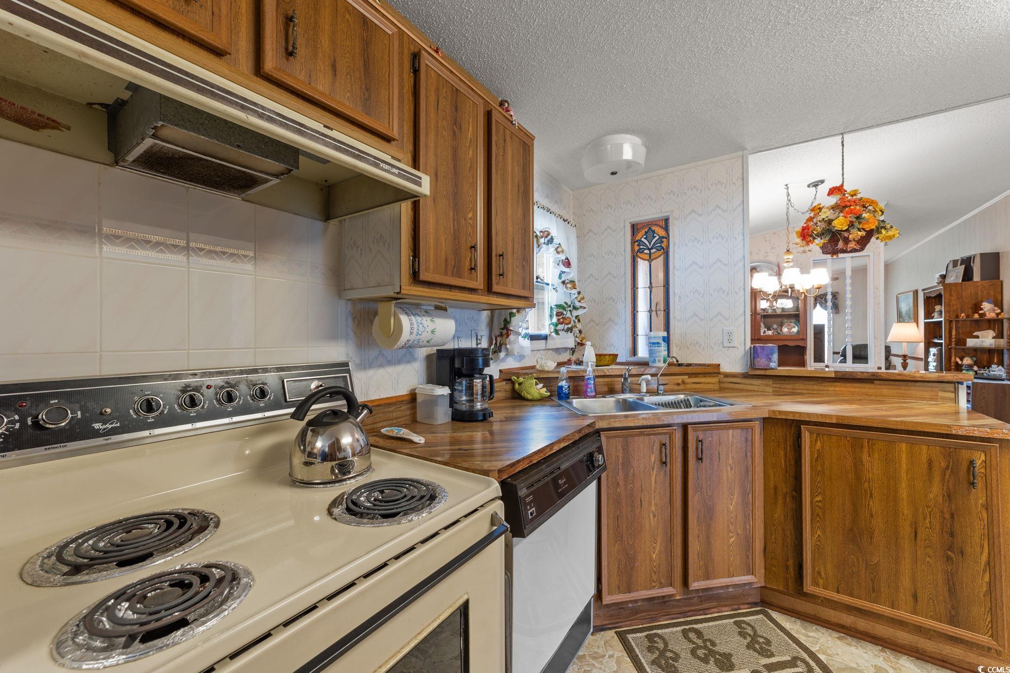 894 South Marlin Circle Murrells Inlet, SC 29576 - Photo 9 of 40 Kitchen featuring wallpapered walls, under cabinet range hood, white appliances, brown cabinets, and a peninsula