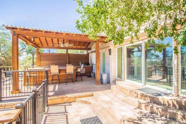 a view of a patio with a table and chairs under an umbrella with large trees